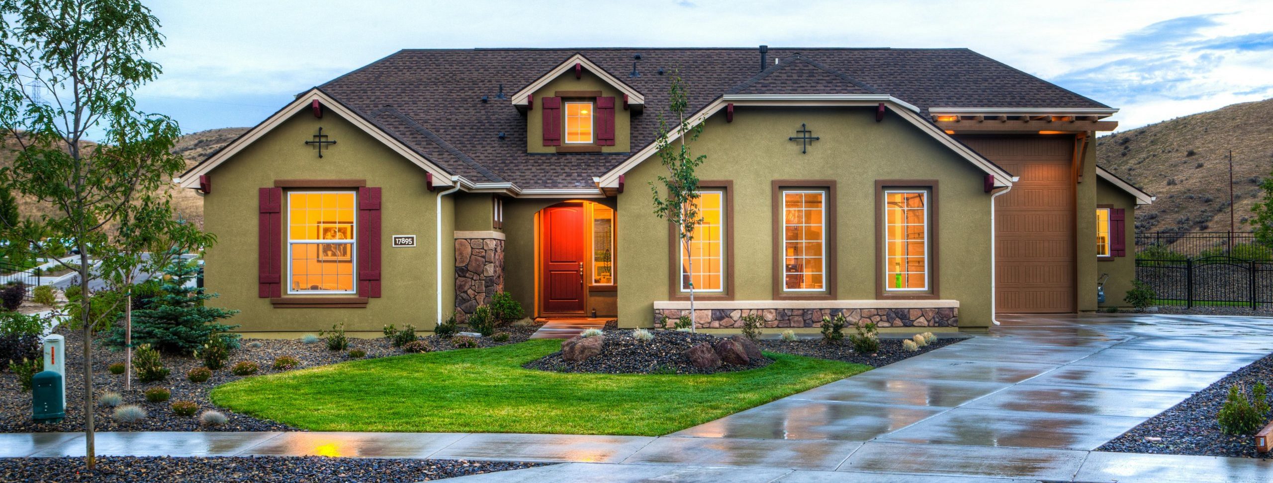 A green home sits nestled in rolling hills, warmly lit in the evening glow.