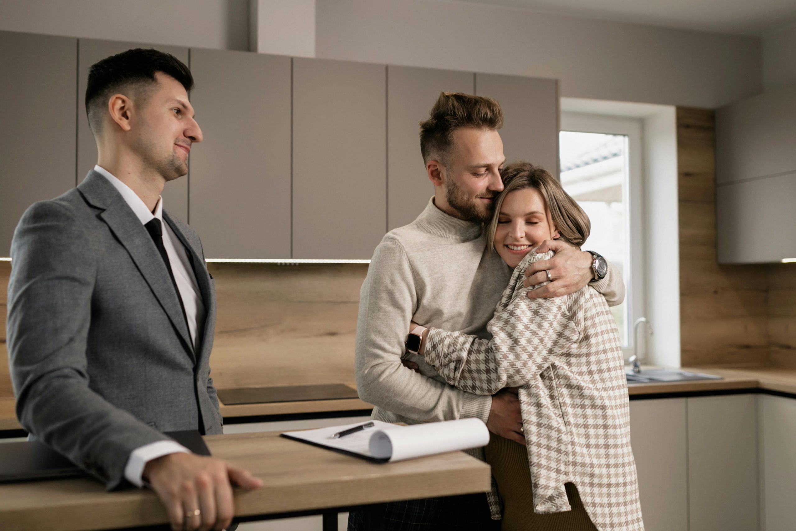 A couple hugging beside a realtor after signing papers to purchase a new home. 