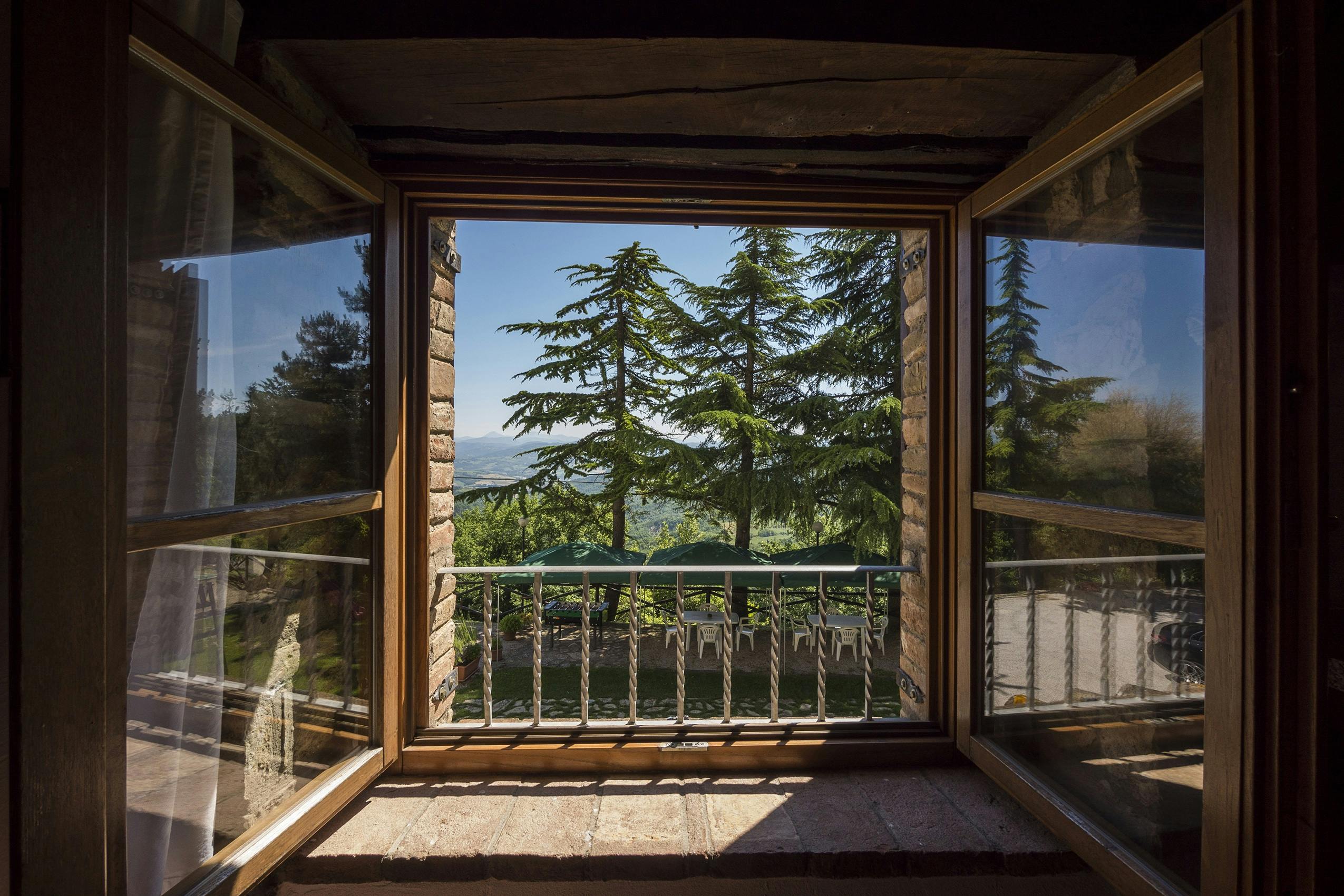 Beautiful view from a wooden balcony, overlooking pine trees and a mountainous valley.