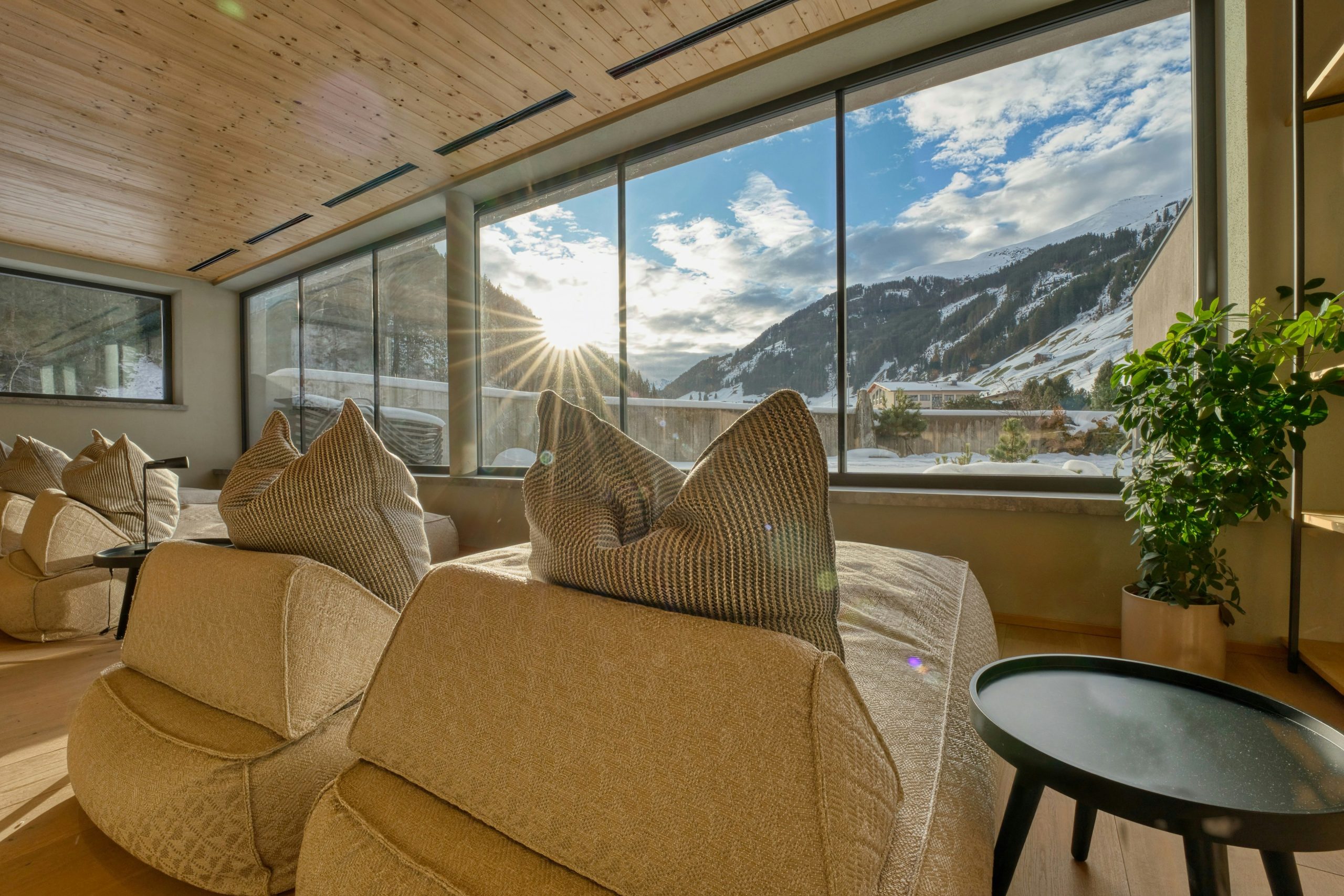 Interior of living room in home, showing a couch inside and a beautiful snowy mountain outside big windows in daytime. 