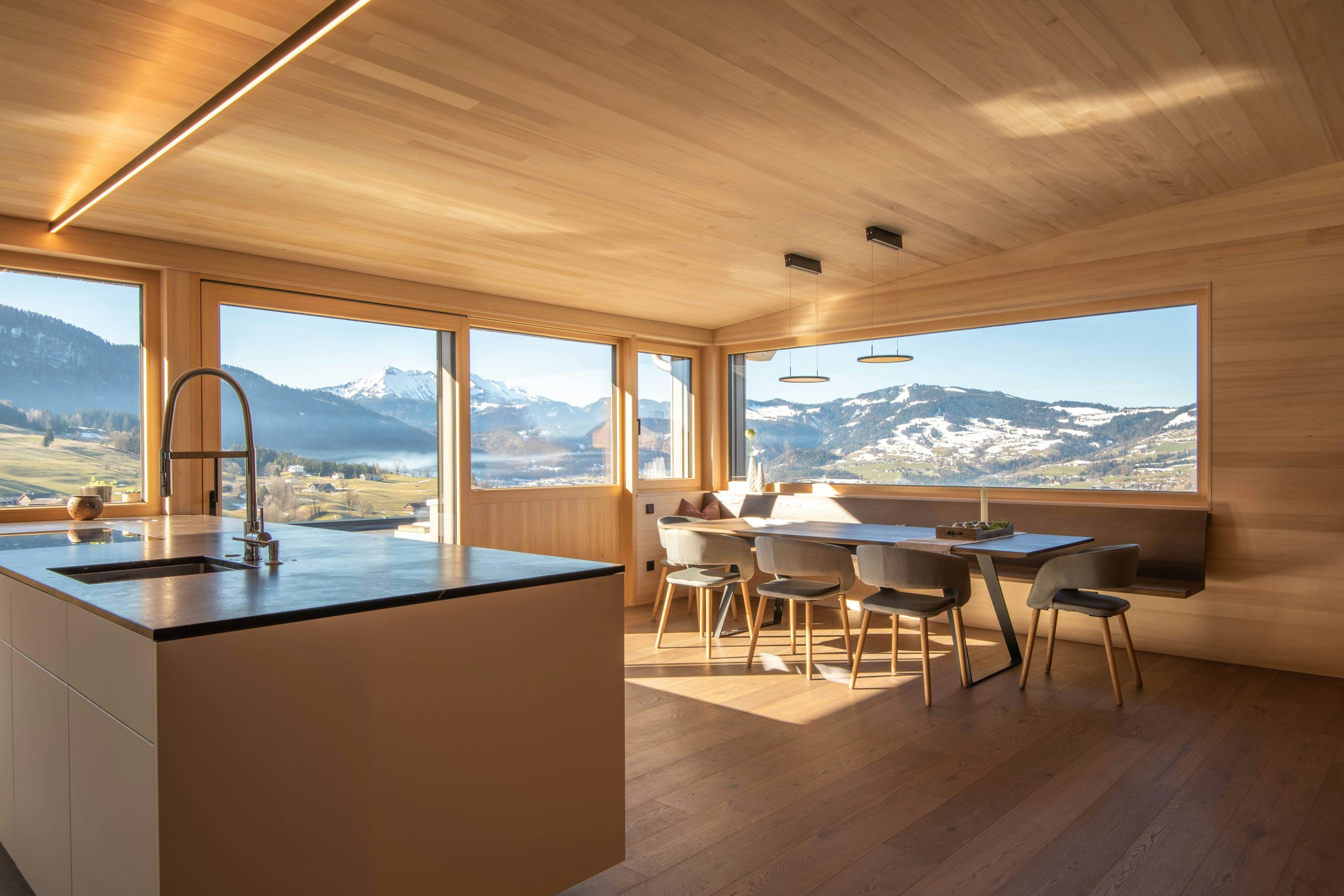 Interior of kitchen and dining room area with panoramic views of some mountains outside.
