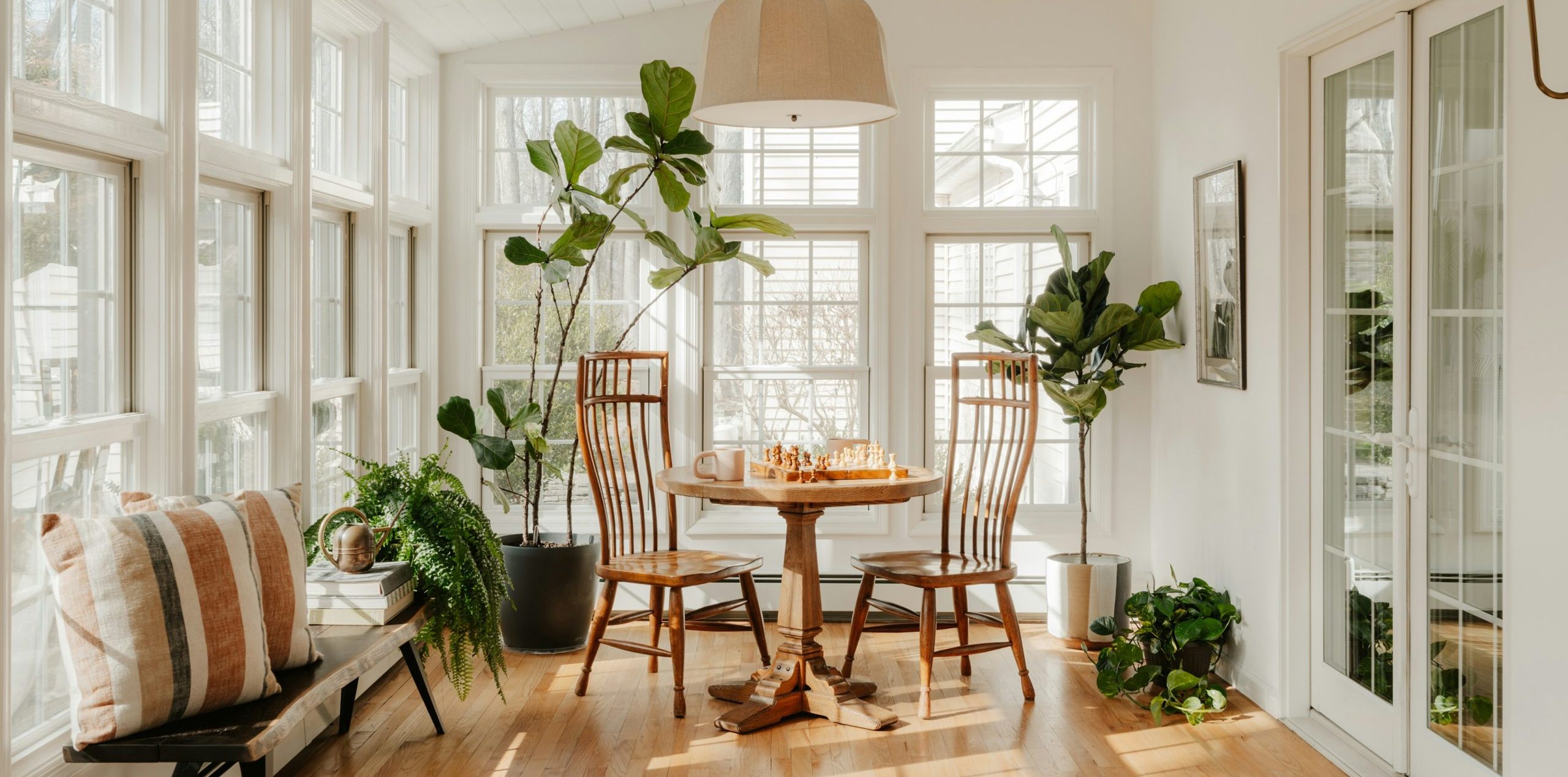 Sunny bright room with a lot of windows, plants and a table and chairs.