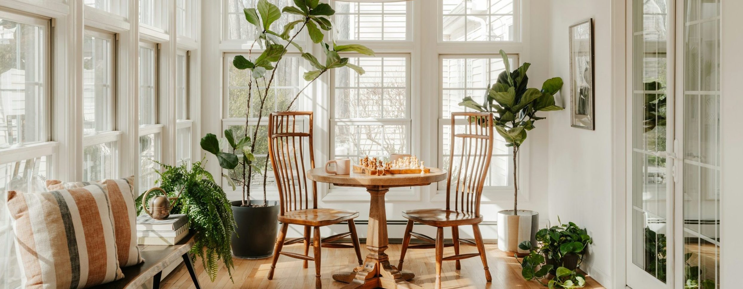 Sunny bright room with a lot of windows, plants and a table and chairs.