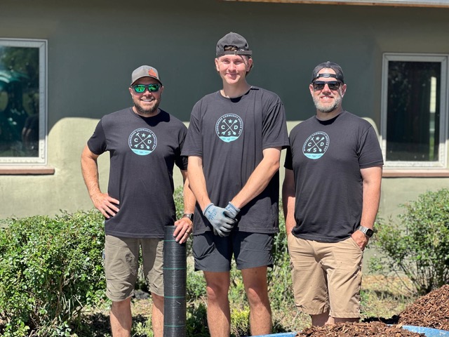 Three volunteers in matching work shirts stand and pose outside for Windermere Community Service Day.