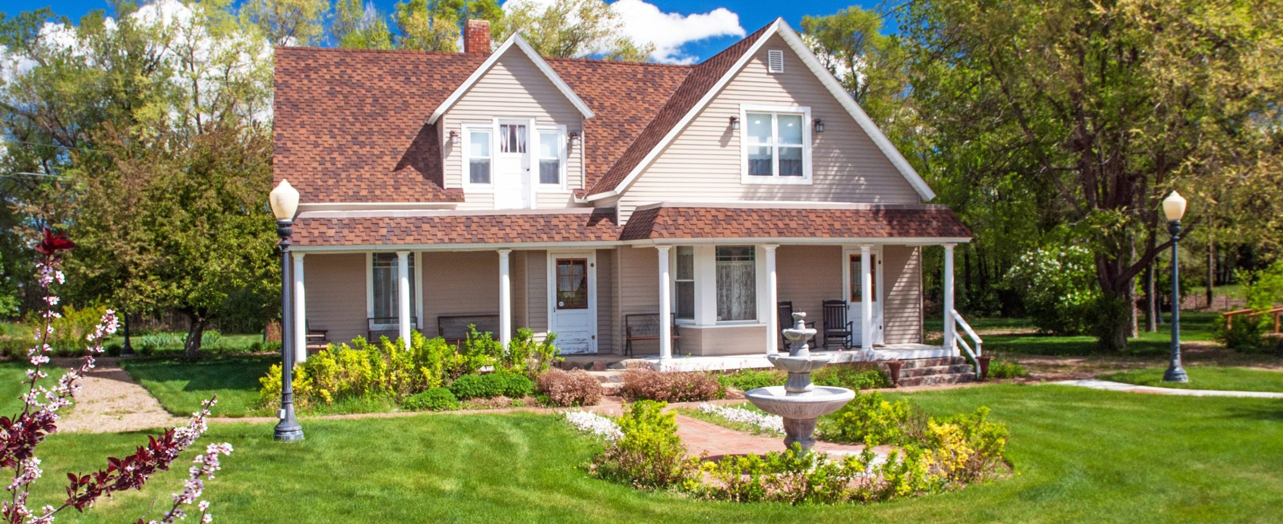The two story house sits on a landscaped yard with a fountain in front.