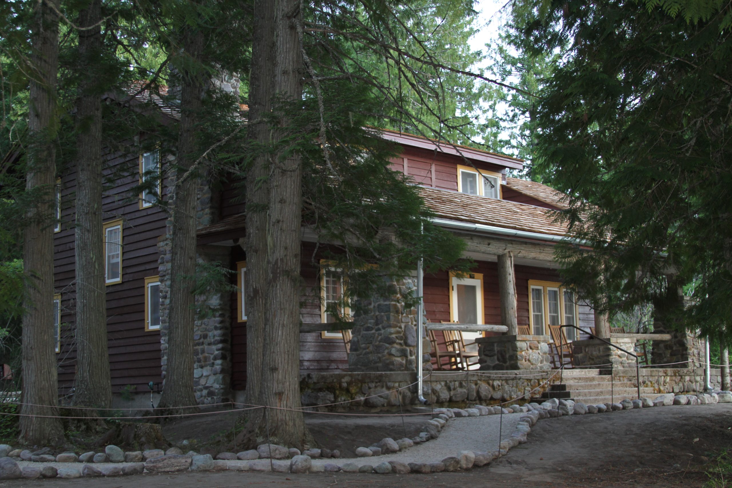 A cabin-style house is surrounded by tall trees and a rocky pathway, perfect for securing during summer home maintenance.